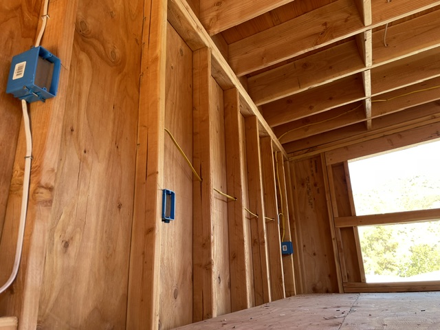Blue electrical boxes and cable runs in unfinished wall framing